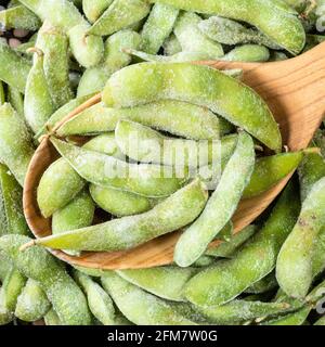 Draufsicht auf gefrorene unreife Edamame-Sojabohnen in der Hülse Holzlöffel Nahaufnahme Stockfoto