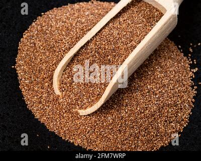 Holzlöffel auf Stapel von Vollkorntaufelsamen auf schwarz Platte Stockfoto