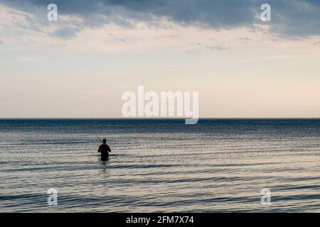 Fischer betraten das Wasser des Meeres auf dem Hintergrund Des violetten - grauen - blauen bewölkten Himmels Stockfoto