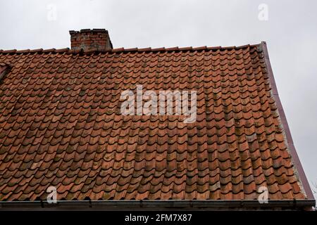 Ein Fragment eines alten, heruntergekommenen, braunen beigefliesten Giebel Dach eines alten Hauses mit einem Ziegelkamin Stapel Ofen mit einer Regenrinne darunter gegen den BA Stockfoto