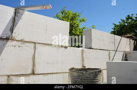 Betonmauerwerk, Betonmauerwerk eines neuen Hauses. Bau einer Wand aus autoklavierten Betonblöcken mit Mörtel, einer Kelle und einer Wasserwaage. Stockfoto