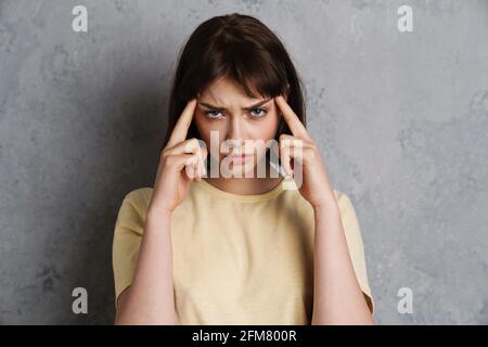 Besorgt gestresste junge Frau, die an einer Migräne leidet, die isoliert ist Grauer Hintergrund Stockfoto
