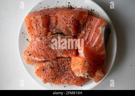 Appetitliche Stücke frischen rohen Lachses mit Gewürzen darauf liegen Eine weiße Platte Stockfoto