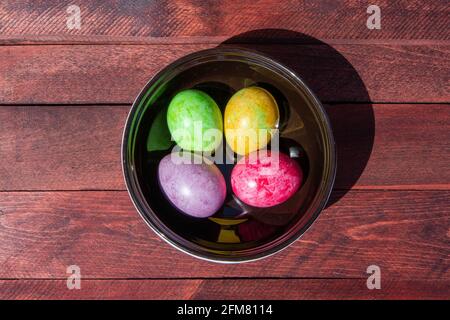 Vier bunte helle ostereier in Keramikschale bleiben auf Rote Holzoberfläche Stockfoto