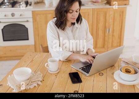 Porträt einer jungen erfolgreichen kaukasischen Freiberuflerin sitzen am Schreibtisch zu Hause. Selbstbewusste Frau arbeitet zu Hause am Laptop online. Stockfoto