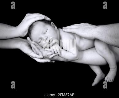 Neugeborener kaukasischer Junge, der mit Vater- und Mutterhänden schläft Isoliert auf schwarzem Hintergrund Stockfoto