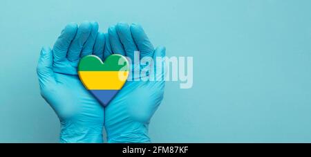 Ärzte Hände tragen chirurgische Handschuhe mit Gabun Flag Herz Stockfoto