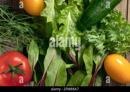 Hintergrund mit verschiedenen Salaten und Gurken, roten und gelben Tomaten auf einer Holzoberfläche. Junge saftige Sprossen der Erbsen oder der Bohnen, Rübentriebe Stockfoto