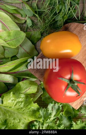 Blur gelbe und rote Tomaten auf Schneidebrett Hintergrund mit verschiedenen Arten von Salaten. Junge saftige Sprossen von Erbsen oder Bohnen, Rübensprossen, grüner Sala Stockfoto