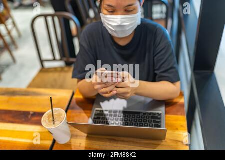 Frau trägt Einwegmaske, während sie Smartphone im Café benutzt Stockfoto