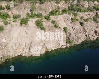 Felsige Ufer des Radon Lake an einem sonnigen Sommermorgen. Luftaufnahme eines alten überfluteten Granitsteinbruchs. Ein malerischer Teich. Stockfoto