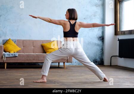 Frau in ihrem Wohnzimmer in Krieger-Yoga-Pose. Stockfoto