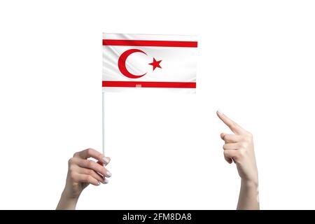 Eine schöne weibliche Hand hält eine Flagge der Türkischen Republik Nordzypern, zu der sie den Finger ihrer anderen Hand zeigt, isoliert auf weißem Hintergrund Stockfoto