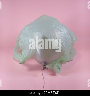 Plastiktüte um den grauen Ballon auf einem weichen rosa Hintergrund gewickelt. Abstraktes Konzept für Umweltverschmutzung und Umweltschutz. Stockfoto