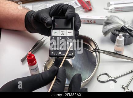 Polizeiwissenschaftler entnimmt DNA-Proben vom Telefon, das an Mord im Labor beteiligt ist, konzeptuelles Bild Stockfoto