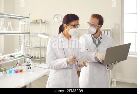 Verschiedene Wissenschaftler in der Gesichtsmaske diskutieren Testergebnisse mit einem Laptop Im Labor Stockfoto