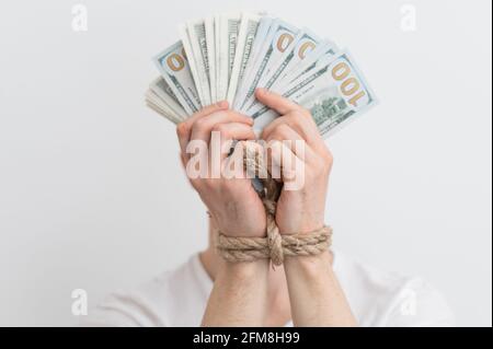 Ein Mann mit gefesselten Händen hält Dollar, Abhängigkeit von Geld, Rückzahlungen, Kreditrückstände Stockfoto