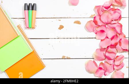 Foto von farbigen Leuchtstofflampen und verschiedenen Notizbüchern auf einem Holzhintergrund weiß und geschmückt mit Rosenblättern.das Foto ist Eine Aufnahme über dem Kopf mit Stockfoto