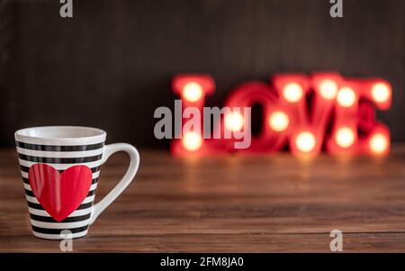 Gestreifte schwarz-weiße Tasse mit rotem Herz auf Holzhintergrund. Valentinstag-Cup. Liebeskonzept Stockfoto