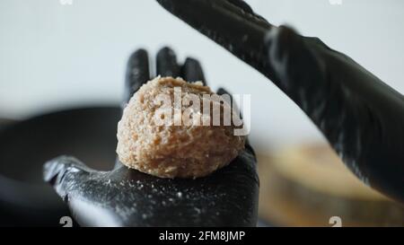 Chefin in schwarzen Handschuhen bereitet Schnitzel zu. Stockfoto