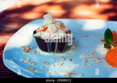 Schlagsahne in einer Schokoladenschale mit Mandeln darauf.Orangen in Scheiben neben dem Teller. Sieht luxuriös aus. Köstliche Wüste. Nahaufnahme. Stockfoto