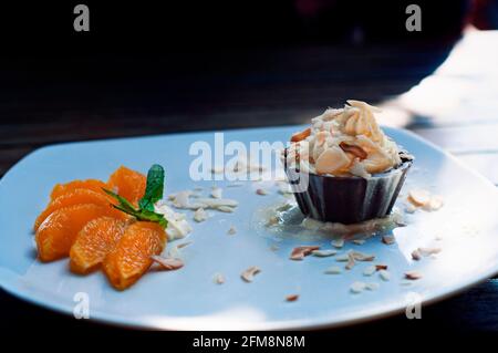 Schlagsahne in einer Schokoladenschale mit Mandeln darauf.Orangen in Scheiben neben dem Teller. Sieht luxuriös aus. Köstliche Wüste. Stockfoto