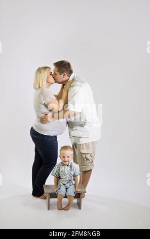 Küssen kaukasischen Paar mit ihrem Sohn auf einem hölzernen sitzen Stuhl isoliert auf weißem Hintergrund Stockfoto