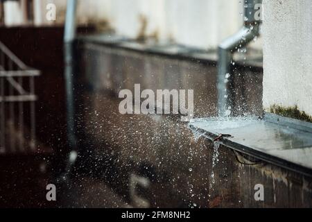 Fallende Regentropfen brechen auf der Kante. Spritzer aus fließendem Wasser. Drainpipe vom Dach eines Gebäudes während eines Regensturms Stockfoto