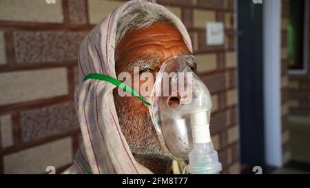 30. April 2021, Jaipur, Rajasthan, Indien. Kranker älterer Mann in Nahaufnahme mit Gesichtssauerstoffmaske, die neben dem Hintergrund der Wand sitzt. COVID 19 Konzept. Stockfoto