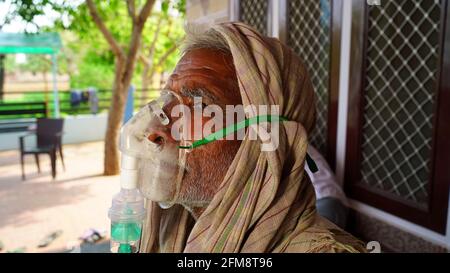 30. April 2021, Jaipur, Rajasthan, Indien. Kranker älterer Mann in Nahaufnahme mit Gesichtssauerstoffmaske, die neben dem Hintergrund der Wand sitzt. COVID 19 Konzept. Stockfoto