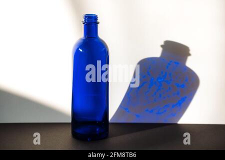 Dunkelblaue Glasflasche auf weißem und schwarzem Hintergrund. Seitenansicht Stockfoto