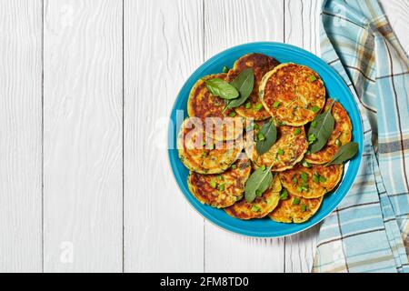 Kichererbsen-Spinat-Pfannkuchen auf einem blauen Teller auf einem weißen Holztisch, horizontale Ansicht von oben, flach liegend, freier Platz Stockfoto