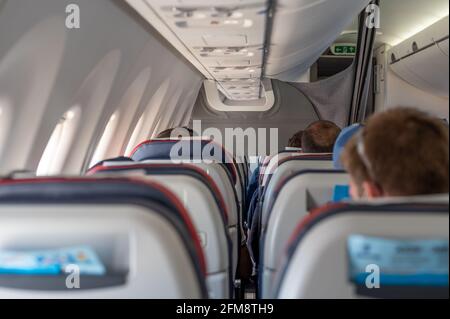 Innenraum eines Verkehrsflugzeugs mit nicht erkennbaren Passagieren auf ihren Sitzen während des Fluges, der vom Flugzeugheck aus geschossen wurde. Passagiere, die in der Armlehne fliegen Stockfoto