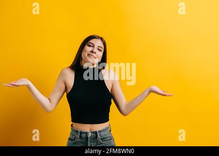 Junge kaukasische Frau mit brünetten Haaren zuckende Missverständnisse, Porträt der emotionalen Frau isoliert auf gelbem Hintergrund mit Copy Space. Stockfoto