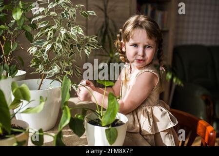 Happy kleine niedliche Baby Mädchen kümmert sich um Zimmerpflanzen. Mädchen Bewässerung und Spritzen Zimmerpflanzen zu Hause Stockfoto