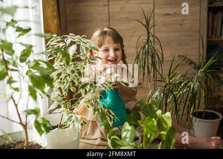 Happy kleine niedliche Baby Mädchen kümmert sich um Zimmerpflanzen. Mädchen Bewässerung und Spritzen Zimmerpflanzen zu Hause Stockfoto