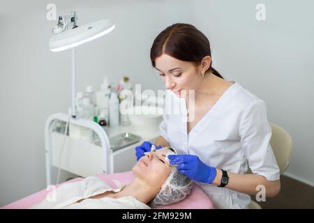 Junge 35-jährige Ärztin in Gummihandschuhen reinigt die Haut einer jungen Frau mit Servietten und Schwämmen. Perfektes Hautkonzept, Reinigung, Spa-Behandlung Stockfoto