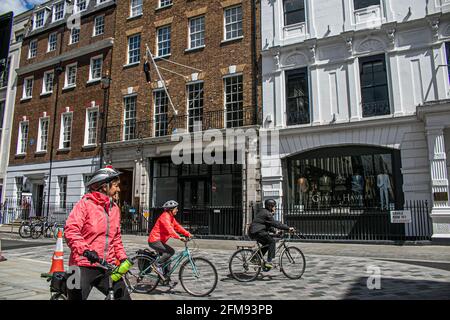 SAVILE ROW LONDON 7. MAI 2021. Eine Gruppe von Radfahrern hält an, um die Skulptur des Künstlers Maurizio Cattelan eines Mannes mit einem Blumenstrauß, der an einer Schlinge hängt, in der Savile Row London zu sehen. Credit amer Ghazzal/Alamy Live News Stockfoto