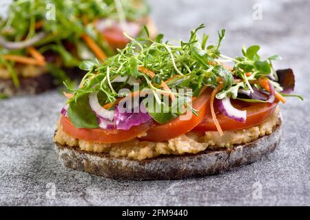 Sandwich geröstetes rustikales Brot mit Kichererbsen-Hummus, Tomatenscheiben, Salat-Mix und Microgreens. Vegetarisches Frühstück. Stockfoto