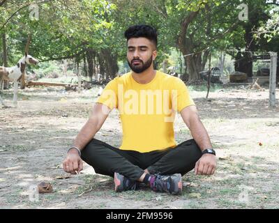 Junger, hübscher Inder in einem gelben T-Shirt, der Yoga macht Im Park an einem sonnigen Tag Stockfoto