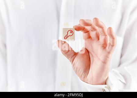 Die männliche Hand hält einen Holzwürfel mit einer Schlüsselikone. Schutz, Schlüssel zum Erfolg oder zum Sperren oder Freischalten im Technologiekonzept. Stockfoto