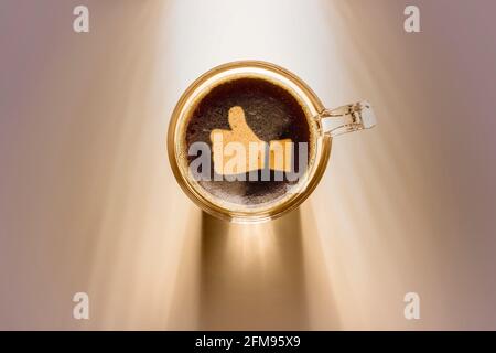 Kaffeetasse mit Daumen nach oben, Draufsicht auf dem Hintergrund mit Sonnenlicht. Stockfoto