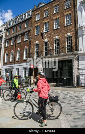 SAVILE ROW, MAYFAIR LONDON 7. MAI 2021. Ein Radfahrer fährt unter dem hängenden Skultpur des Künstlers Maurizio Cattelan eines Mannes, der einen Blumenstrauß in der Savile Row London an einer Schlinge hält. Credit amer Ghazzal/Alamy Live News Stockfoto