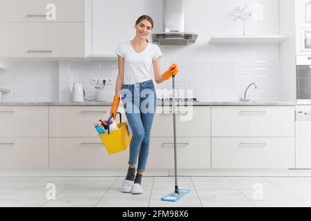 Schöne junge Frau, die mit Mopp und Waschmittel steht und sich auf die Reinigung vorbereitet. Konzept der Reinigung in der Küche. Stockfoto