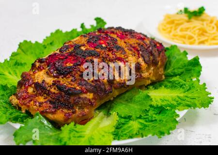 Ein großes Stück gehacktes Schweinefleisch, im Ofen gekocht, im Ofen gebacken, auf grünen Salatblättern, Nahaufnahme. Stockfoto