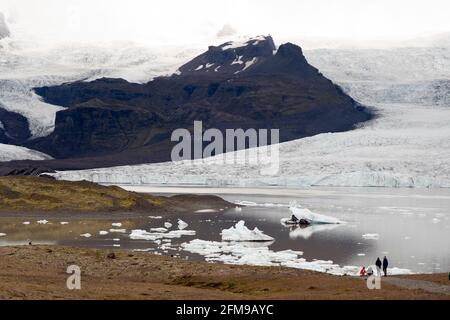 Eis vom Breioamerkurjokull-Gletscher (hinten) kält sich in den Fjallsarlon-Gletschersee im Vatnajokull-Nationalpark, Island. Stockfoto