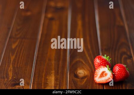 Nahaufnahme von zweieinhalb Erdbeeren isoliert auf Dunkles Holz Stockfoto