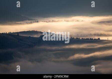 Neblige Morgenlandschaft über dem Dorf Bucovina. Sonnenaufgang über den nebligen Hügeln der rumänischen Landschaft Stockfoto