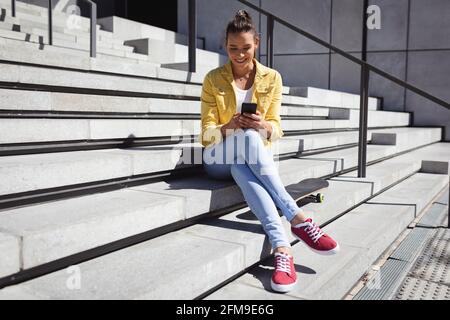 Lächelnde kaukasische Frau, die auf Treppen sitzt und Smartphone benutzt Stockfoto