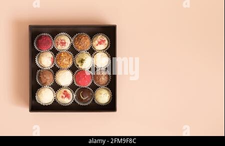 Trüffel in einer Schachtel auf einem rosa Hintergrund. Verschiedene Bonbons oder Energiebälle. Hausgemachte Süßigkeiten. Platz zum Kopieren, Draufsicht, flach liegend. Stockfoto